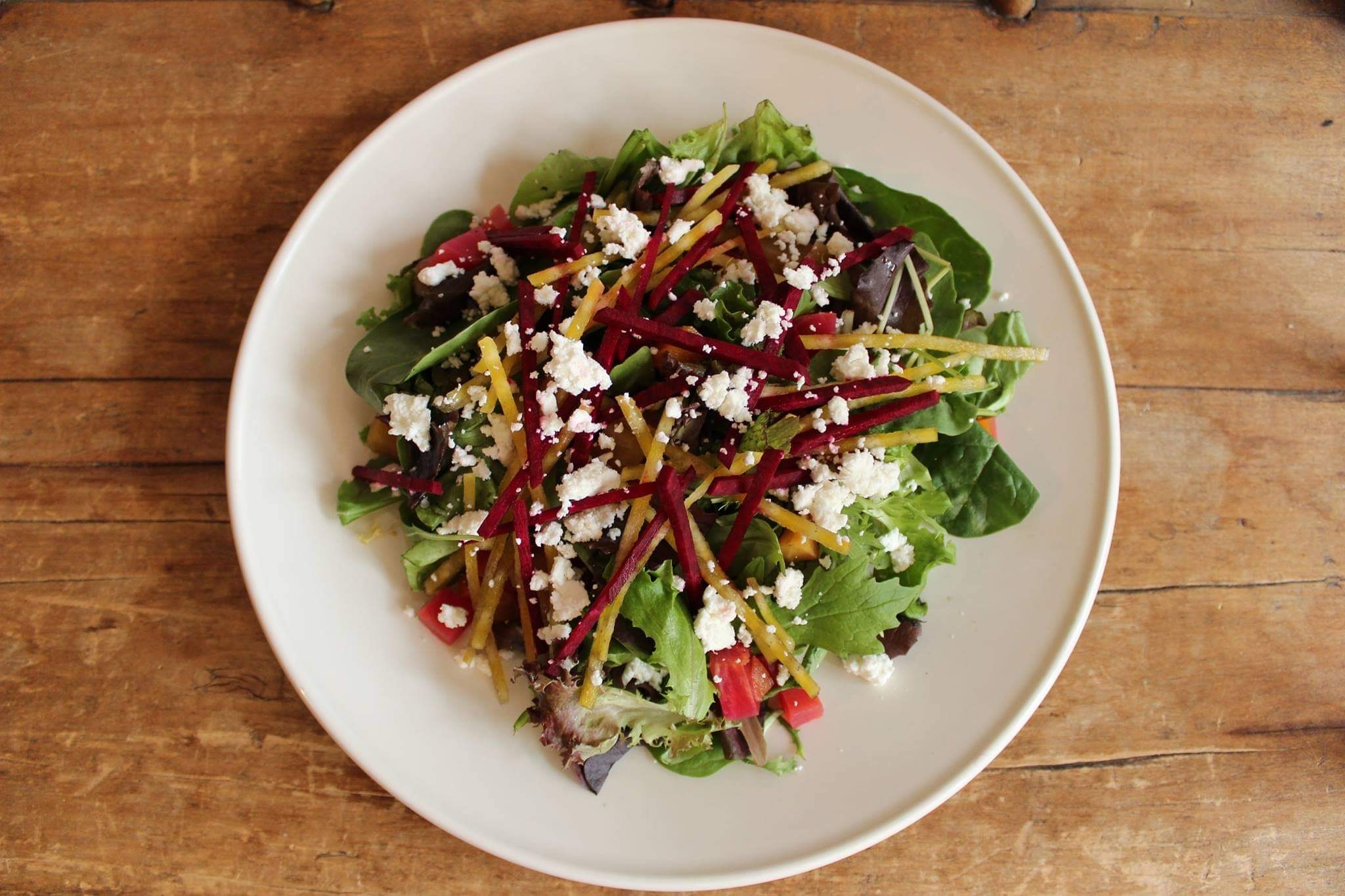 A fresh garden salad with beets, goat cheese, and tomatoes on a bed of greens.