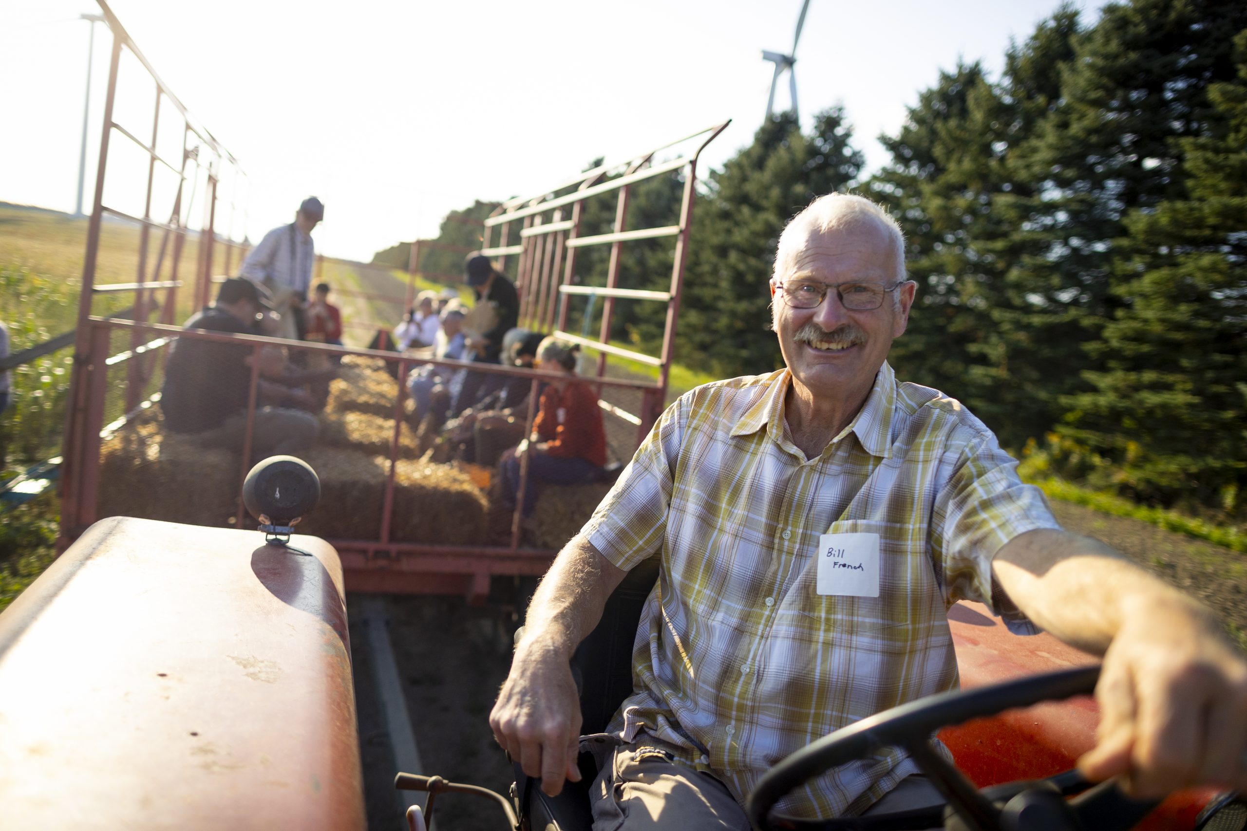 Older man driving a tractor with a trailer full of people