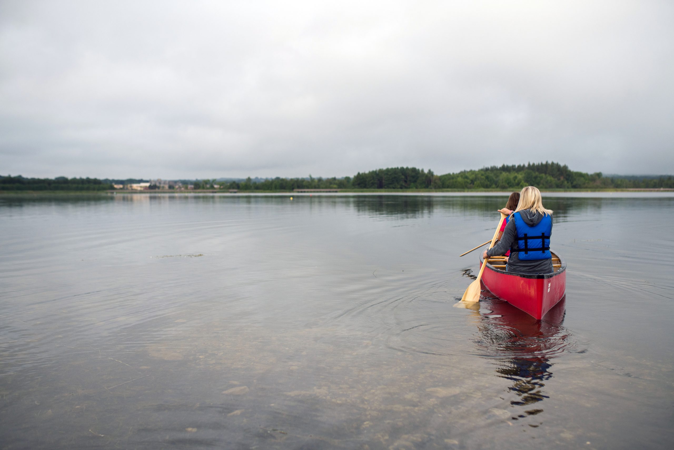 two ladies on a lake rowing a red kayak