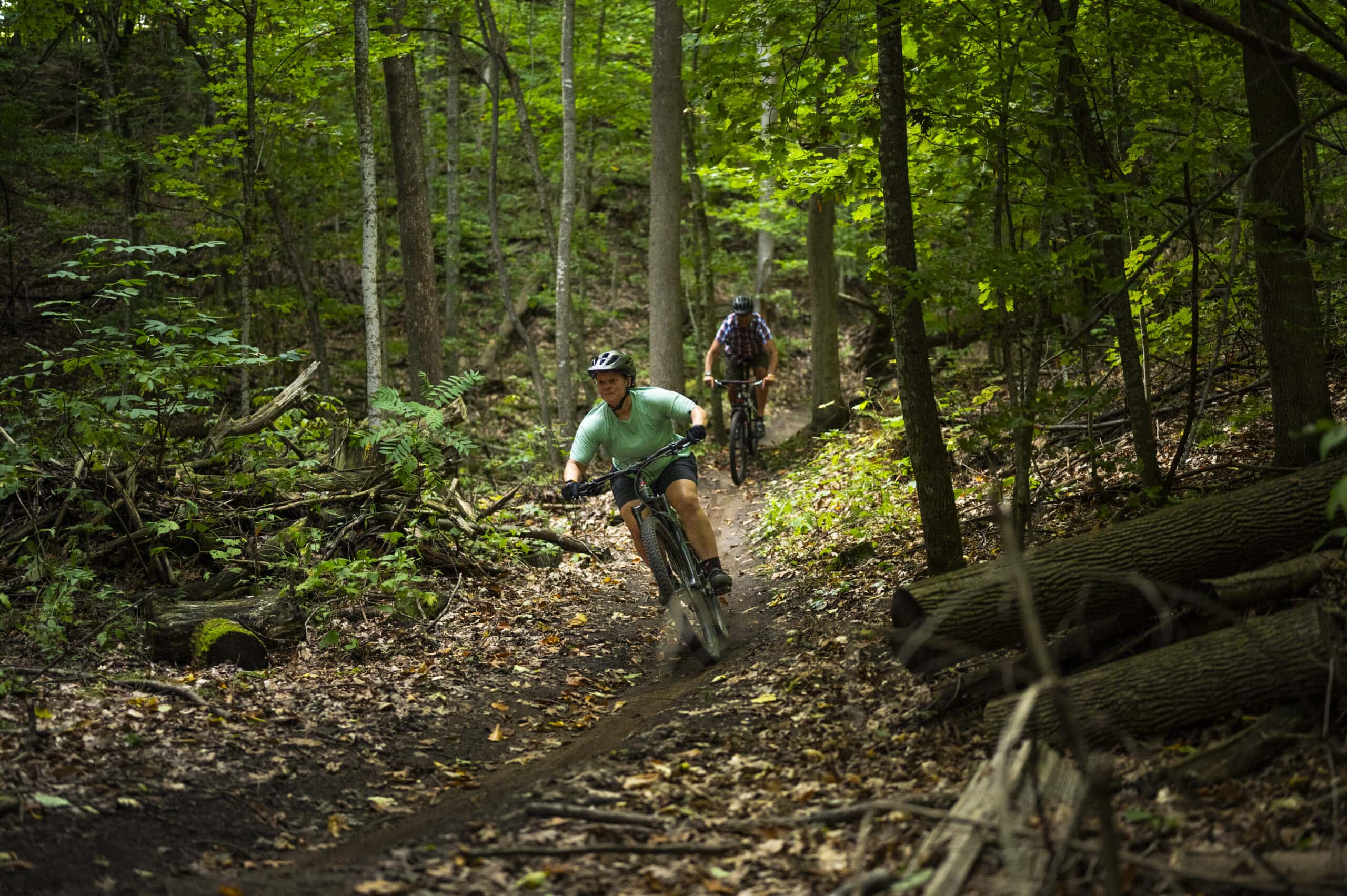 Two cyclers hiking in lush forest.